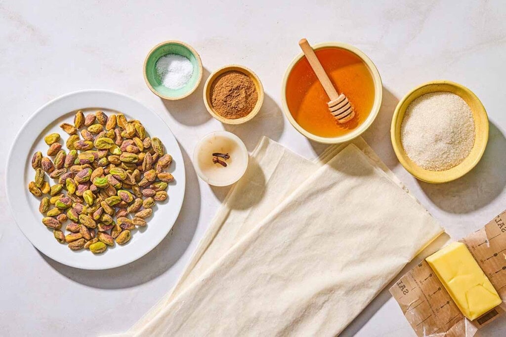 Ingredients for baklava bark including phyllo dough, pistachios, sugar, butter, honey, ground cinnamon, salt, andwhole cloves.