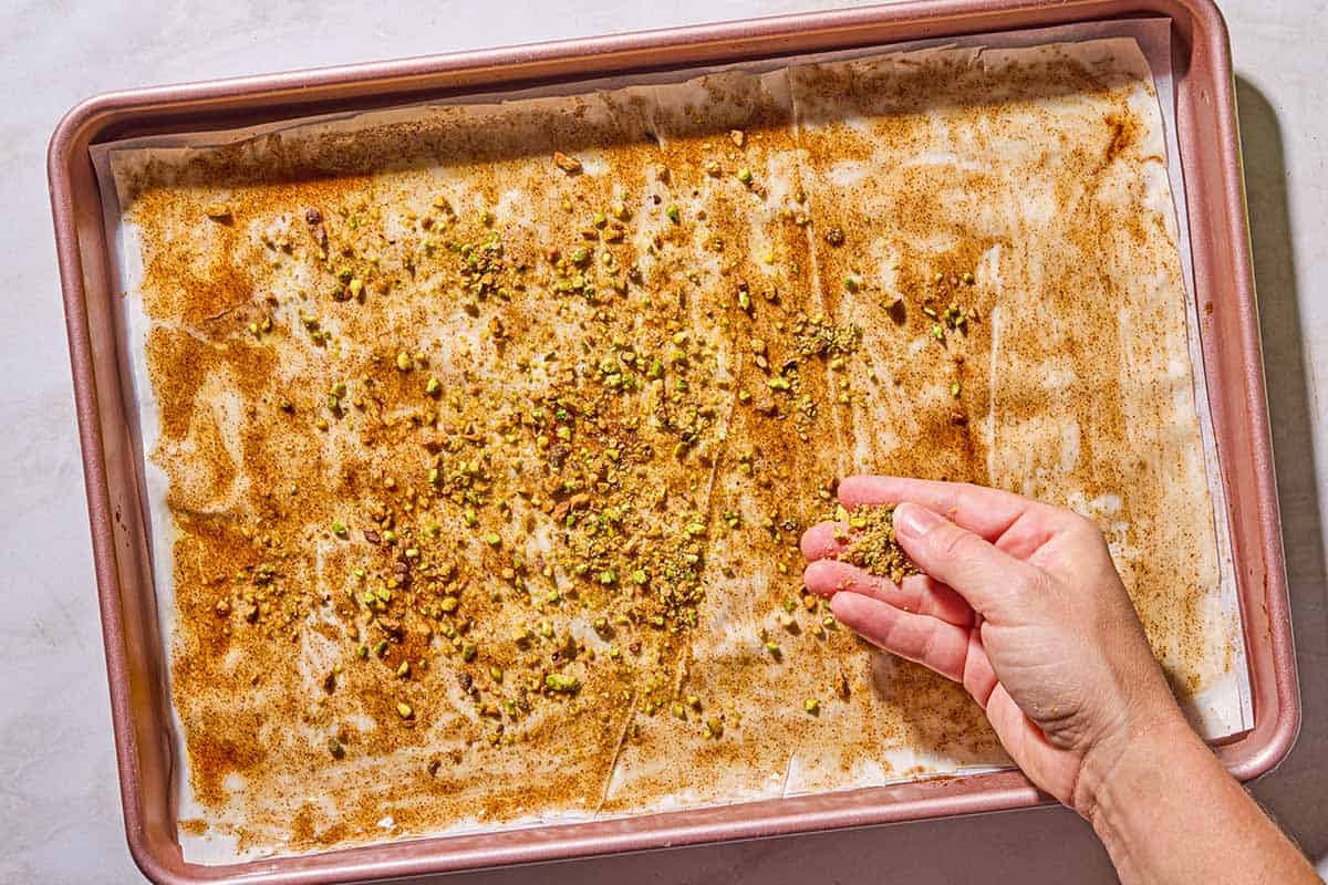 The nut mixture for the baklava bark being sprinkled onto the honey mixture and phyllo dough lining the sheet pan.