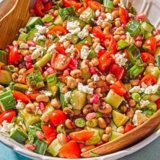 The black eyed pea salad in a bowl with wooden serving utensils.