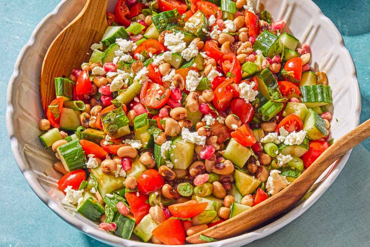 The black eyed pea salad in a bowl with wooden serving utensils.
