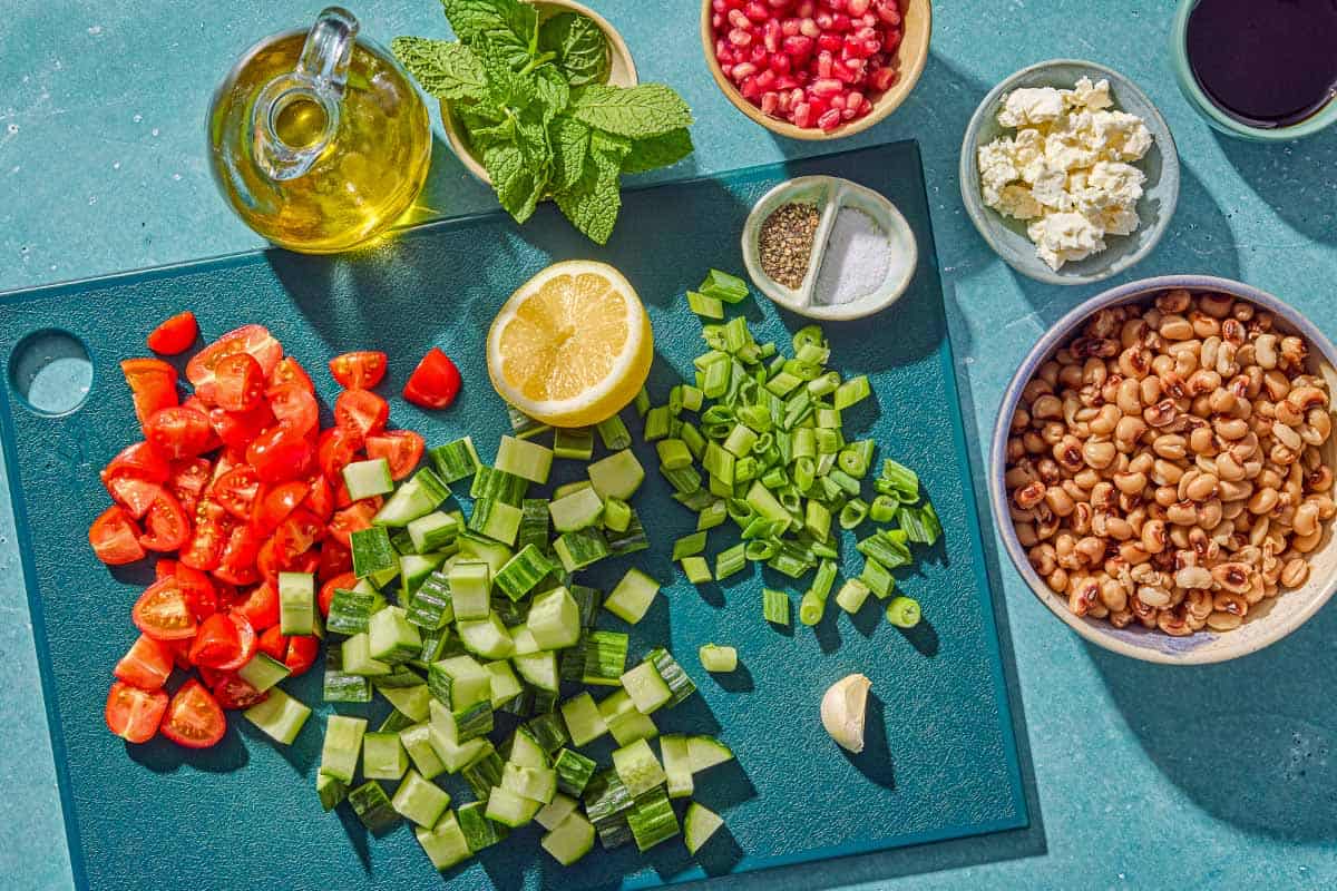 Ingredients for black eyed pea salad including black eyed peas, crumbled feta, grape tomatoes, cucumber, pomegranate arils, green onions, mint, pomegranate molasses, lemon, olive oil, garlic, salt and pepper.
