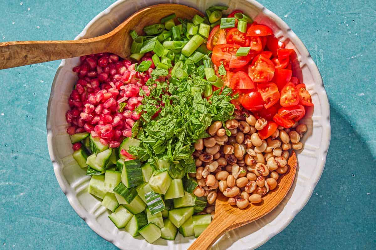 The black eyed pea salad in a bowl with wooden serving utensils just before being mixed together.