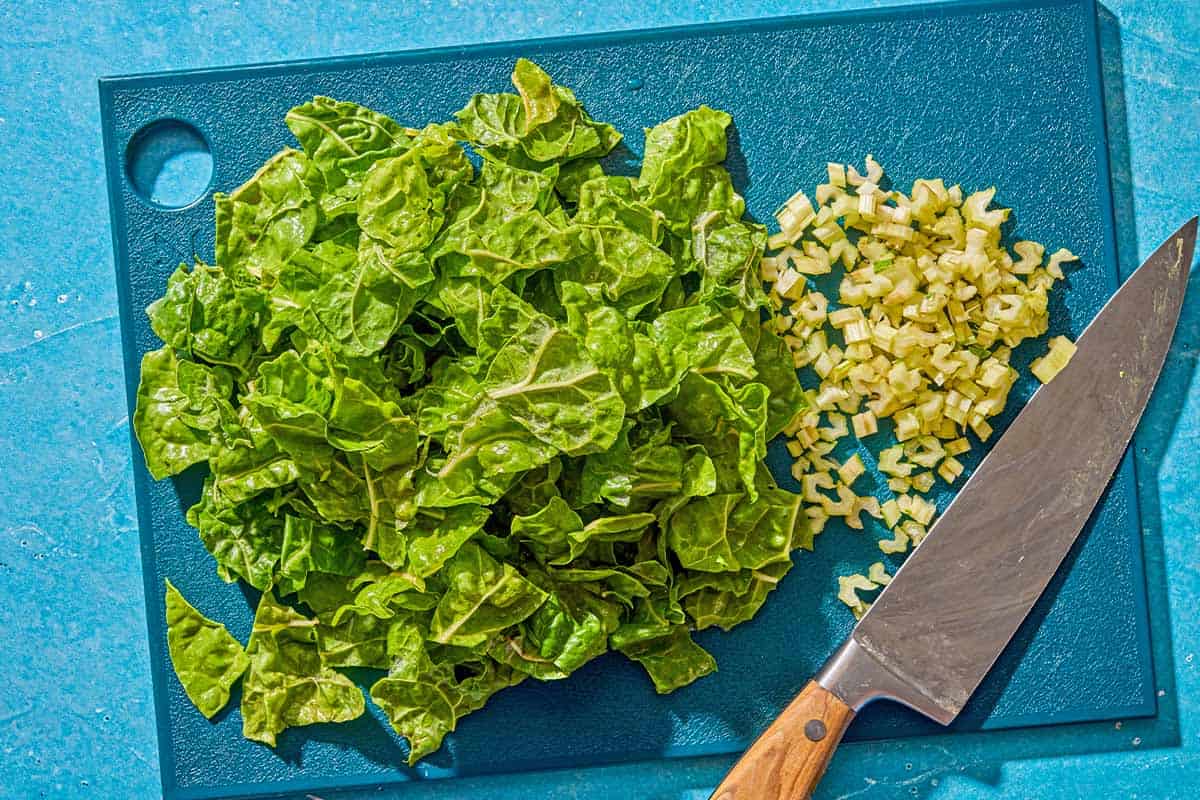 Chopped Swiss chard and the chopped stems on a cutting board with a knife.
