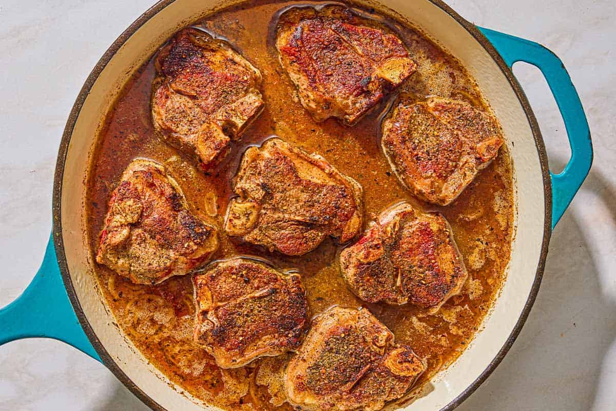 Several braised lamb chops in a braising pan.