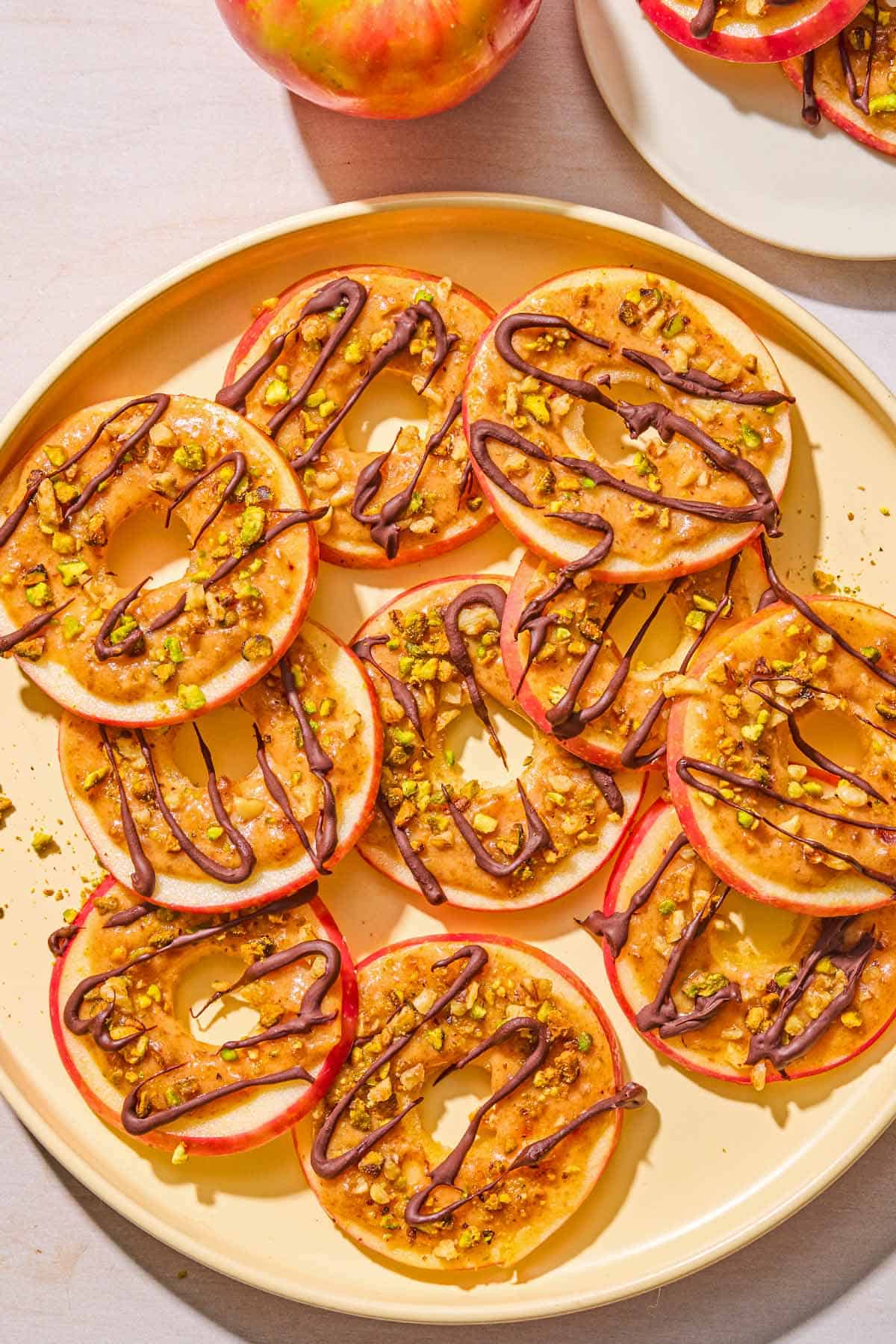 Several caramel apple slices on a platter. Next to this is an apple and a plate with more of the caramel apple slices.