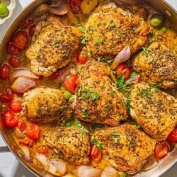 The chicken provencal in a skillet. Next to this are bowls of chopped herbs and green olives.