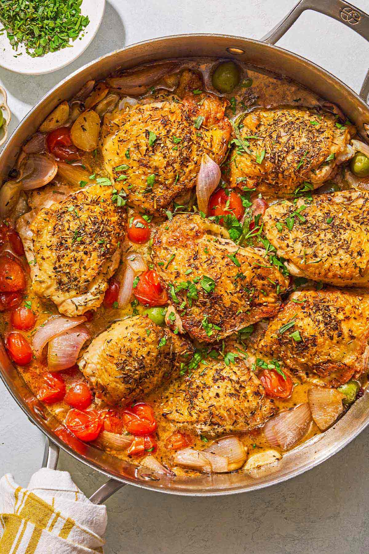 The chicken provencal in a skillet. Next to this is a bowl of chopped herbs.