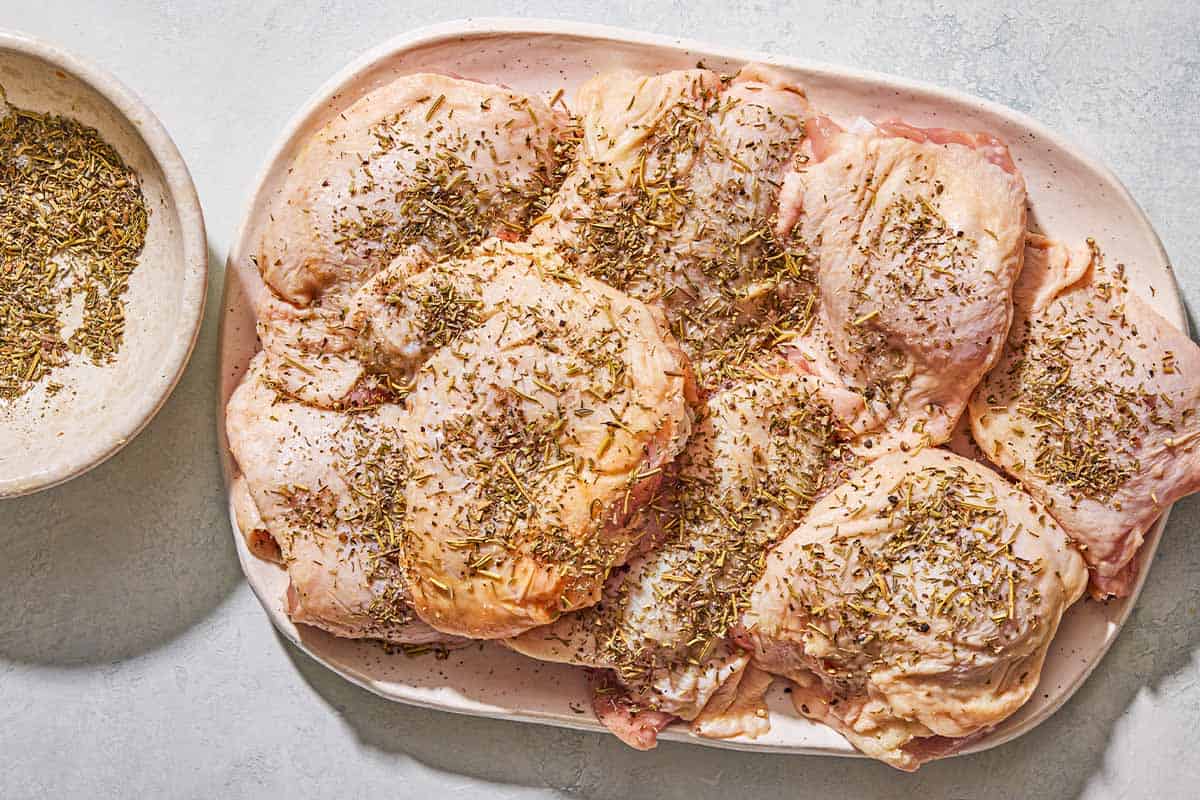 The seasoned, uncooked chicken thighs for the chicken provencal on a platter. Next to this is a bowl of the seasoning.