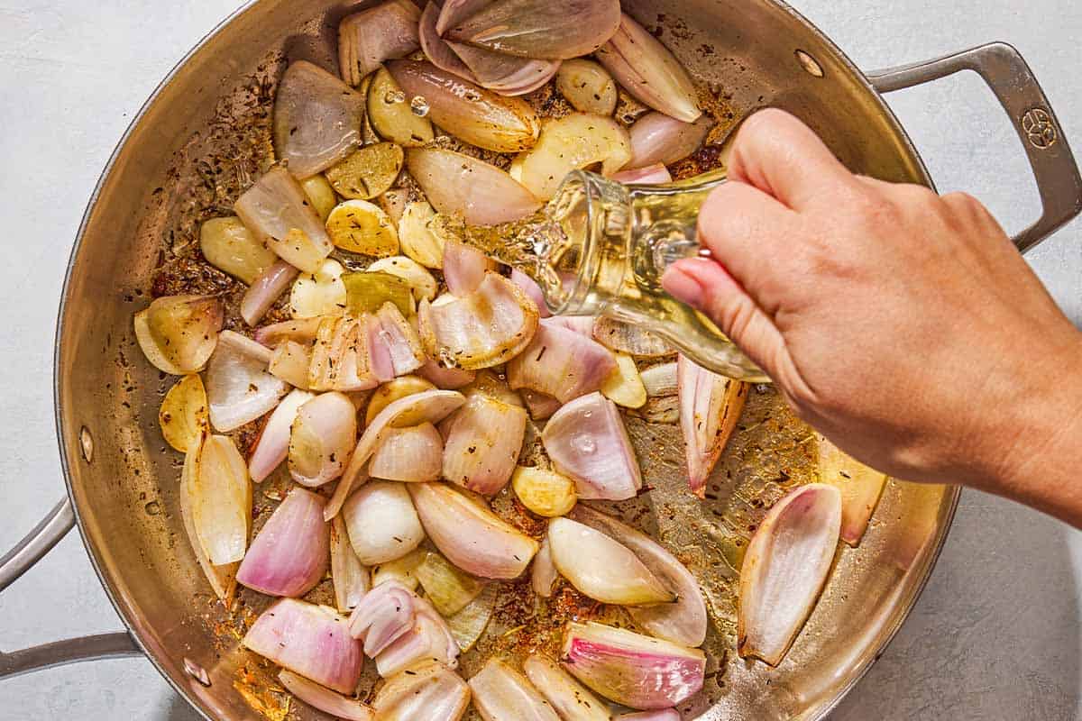 The white wine being poured over the aromatics for the chicken provencal in the skillet.