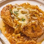 A serving of french onion chicken on a plate with a knife and fork.