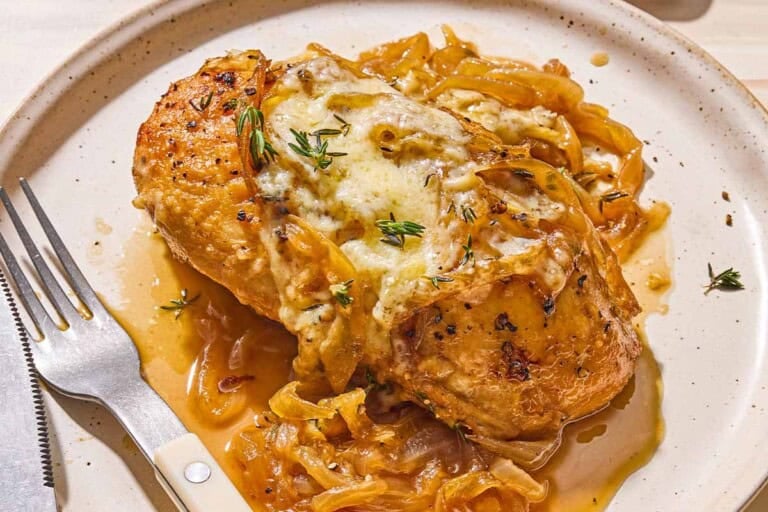 A serving of french onion chicken on a plate with a knife and fork.