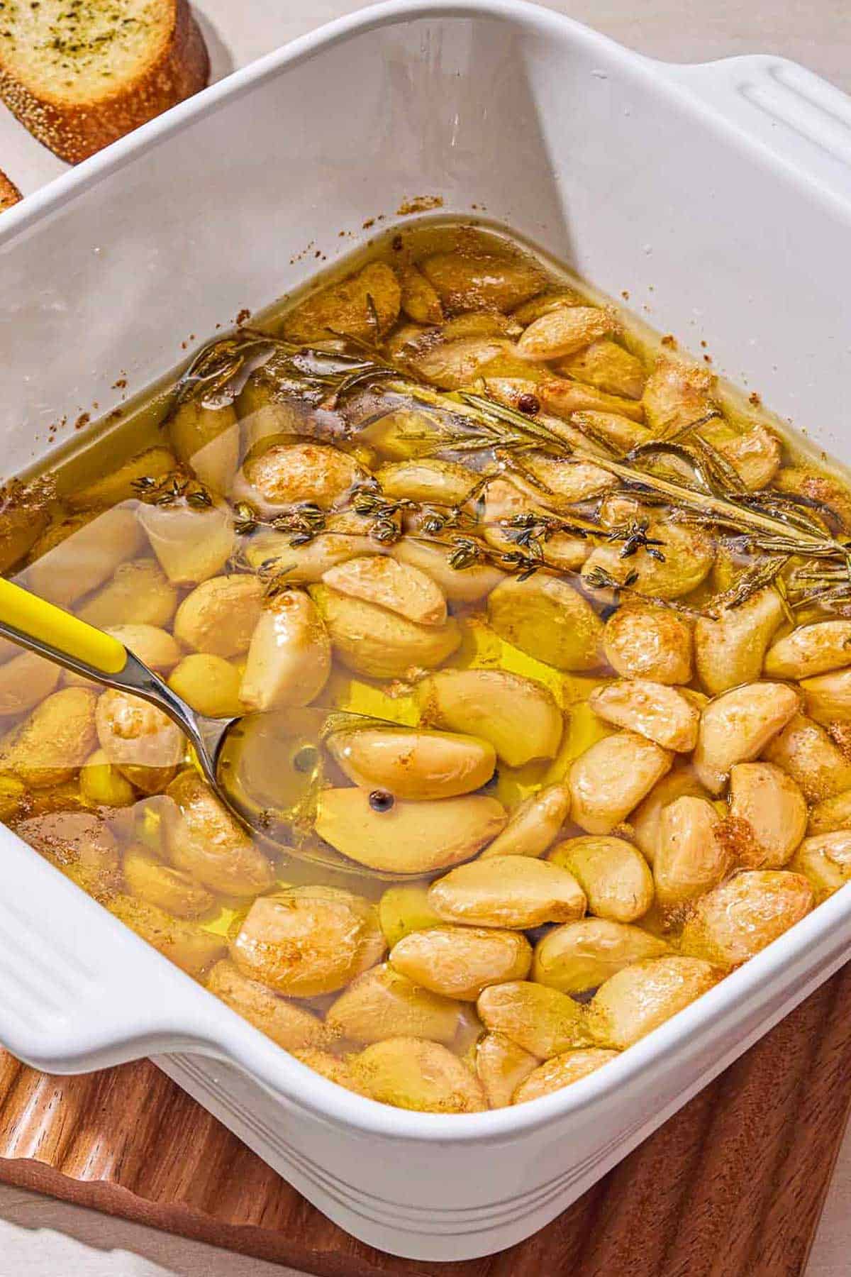 Garlic confit in a square baking dish with a spoon.