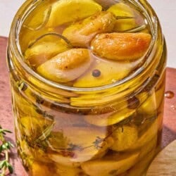 Garlic confit in a jar on a wooden tray.