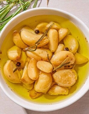 Garlic confit in a jar. Next to this are fresh sprigs of thyme and rosemary.