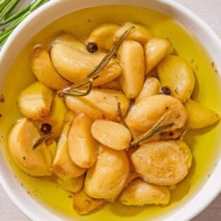 Garlic confit in a jar. Next to this are fresh sprigs of thyme and rosemary.