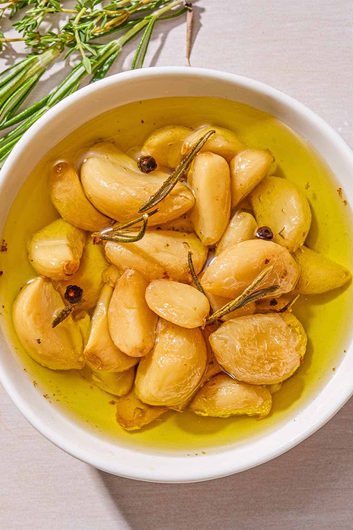 Garlic confit in a jar. Next to this are fresh sprigs of thyme and rosemary.