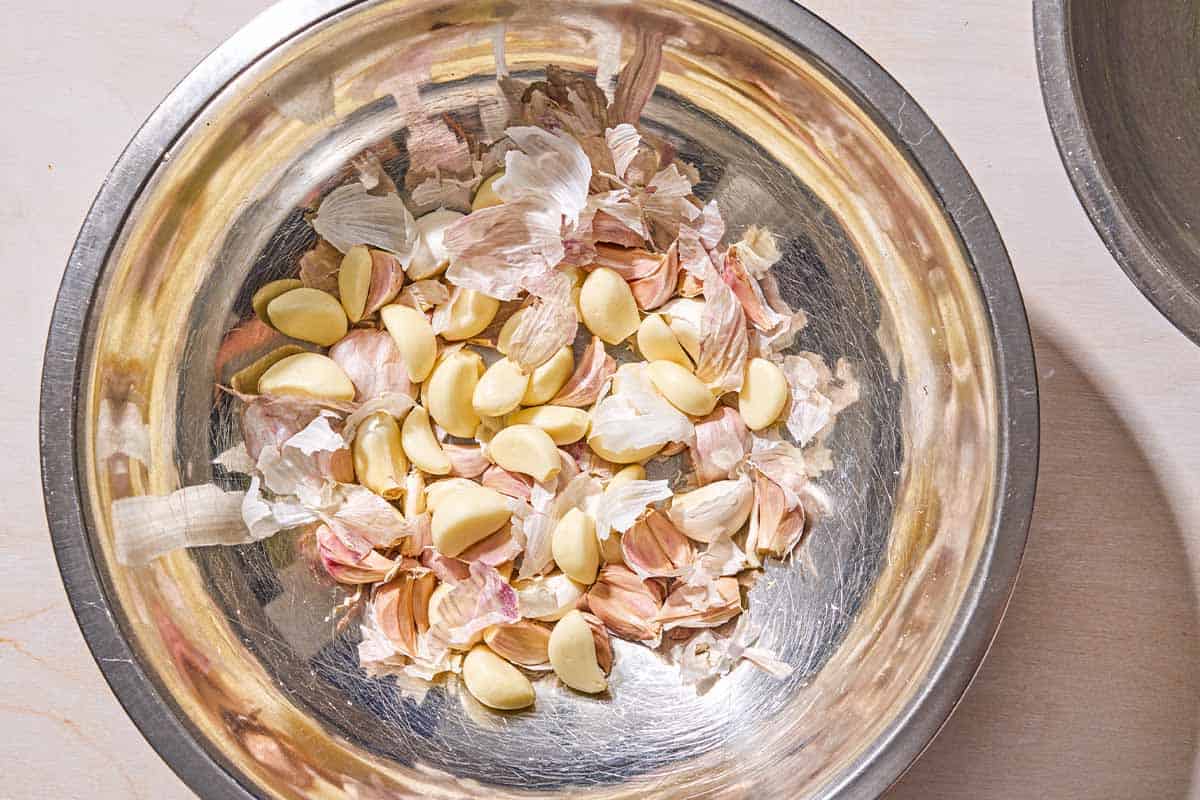 Peeled garlic cloves and the skins in a metal bowl.