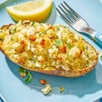 A twice baked potato on a plate with a fork and a lemon wedge.