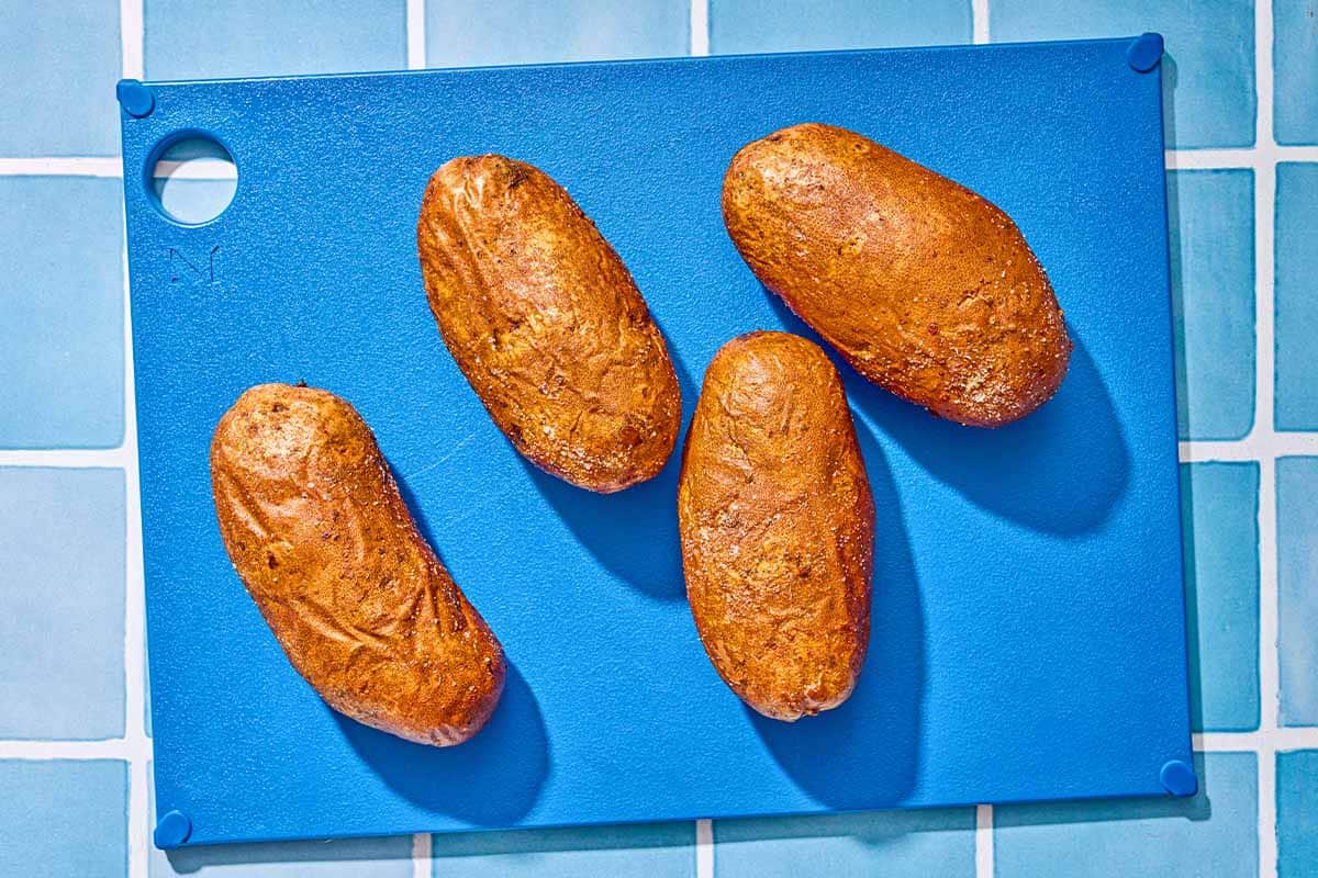 Four baked potatoes on a cutting board.