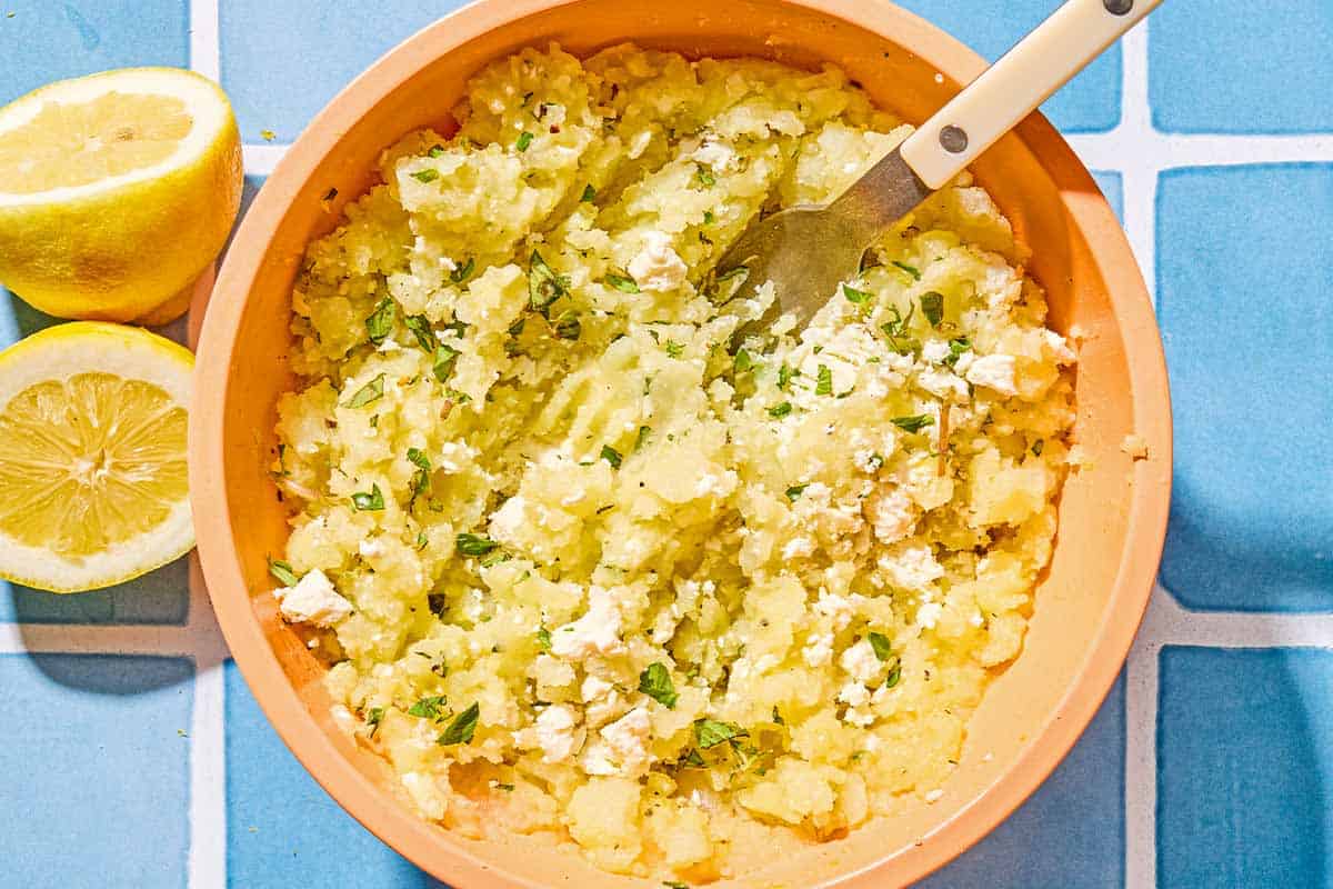 The filling for the twice baked potatoes in a bowl with a fork. Next to this are two lemon halves.
