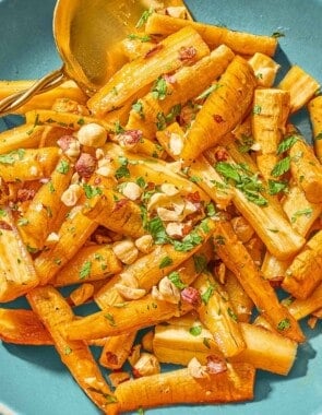 Roasted parsnips coated in a honey glaze and topped with hazelnuts and parsley in a serving bowl with a spoon.
