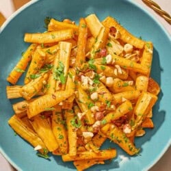 Roasted parsnips coated in a honey glaze and topped with hazelnuts and parsley in a serving bowl next to this is a bowl of roasted hazelnuts.
