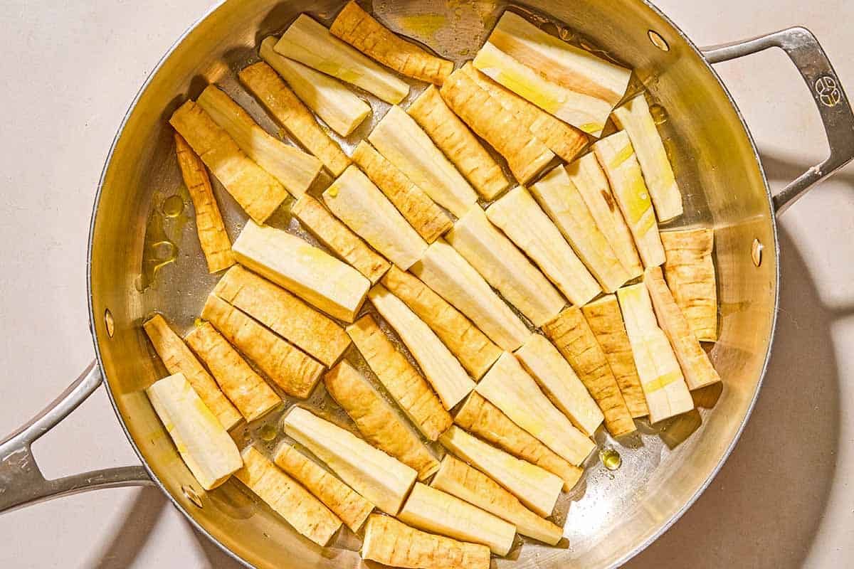 The uncooled parsnips drizzled in olive oil arranged in a single layer in a skillet.