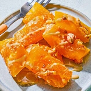 Kabak Tatlisi drizzled with tahini and topped with walnuts on a plate with a fork.