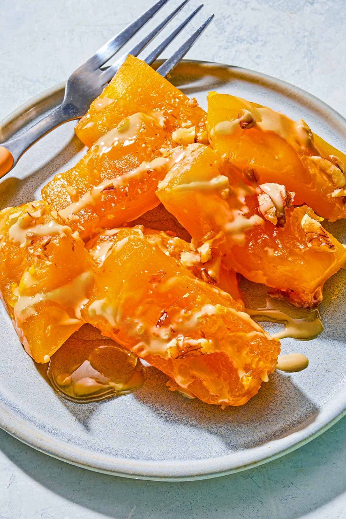 Kabak Tatlisi drizzled with tahini and topped with walnuts on a plate with a fork.