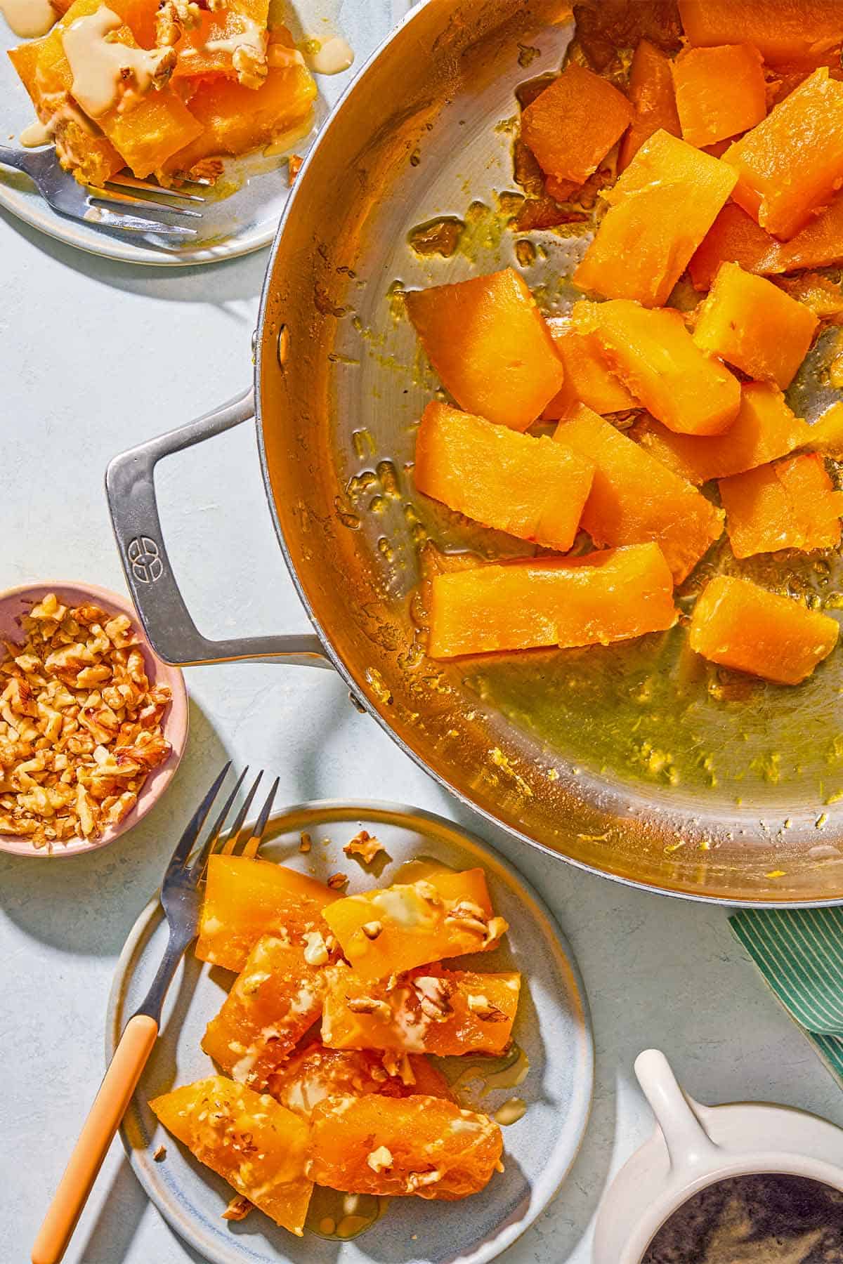 Kabak Tatlisi in a large saucepan. Next to this are two servings of the recipe on plates with forks, a bowl of walnuts, and a cup of coffee.