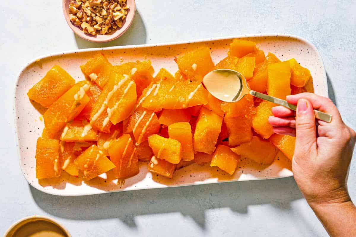 The candied pumpkin on a platter being drizzled with tahini. Next to this is a bowl of walnuts.