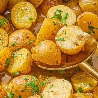 A close up of roasted baby potatoes topped with chopped parsley with a serving spoon.