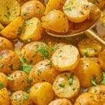 A close up of roasted baby potatoes topped with chopped parsley with a serving spoon.