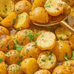 A close up of roasted baby potatoes topped with chopped parsley with a serving spoon.