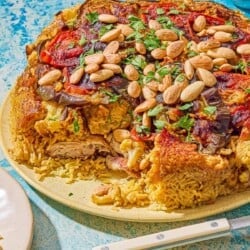 The maqluba on a platter next to a plate, a utensil and a small bowl of blanched almonds.