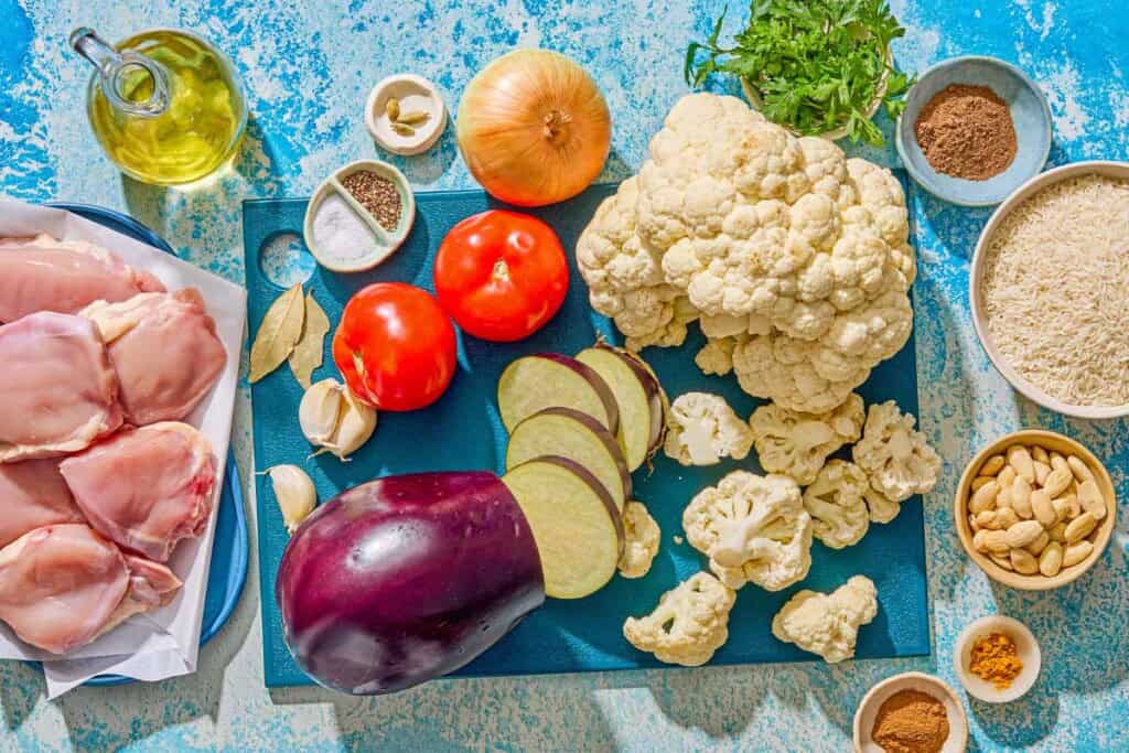 Ingredients for the maqluba recipe including rice, salt, pepper, eggplant, olive oil, cauliflower, chicken thighs, allspice, cinnamon, onion, garlic, bay leaves, cardamom pods, tomatoes, ground turmeric, and blanched almonds.