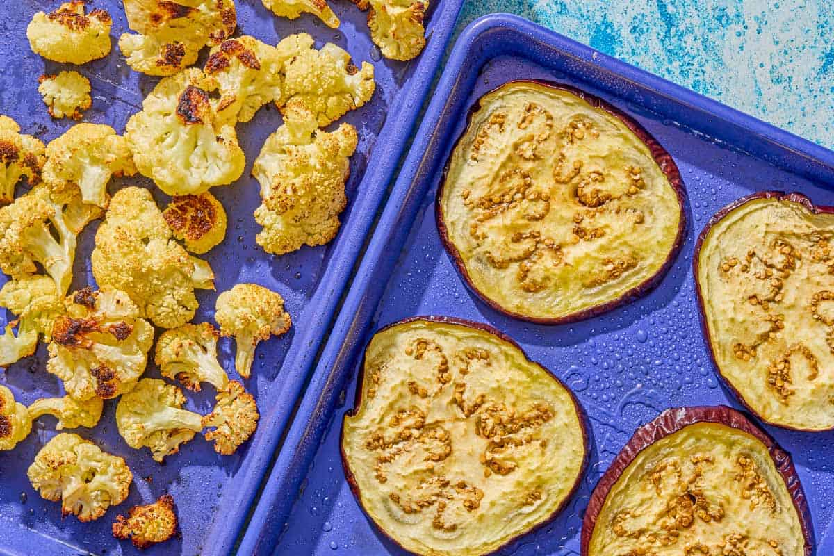 A sheet pan with roasted cauliflower next to a sheet pan with roasted eggplant slices.