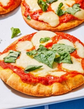 A close up of a pita pizza topped with fresh basil, with two more pizzas in the background.