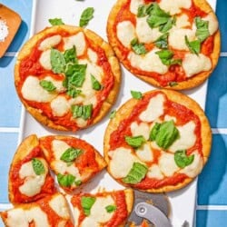 Four pita pizzas topped with fresh basil on a patter with a pizza slicer. One pita pizza is sliced into 4 pieces.