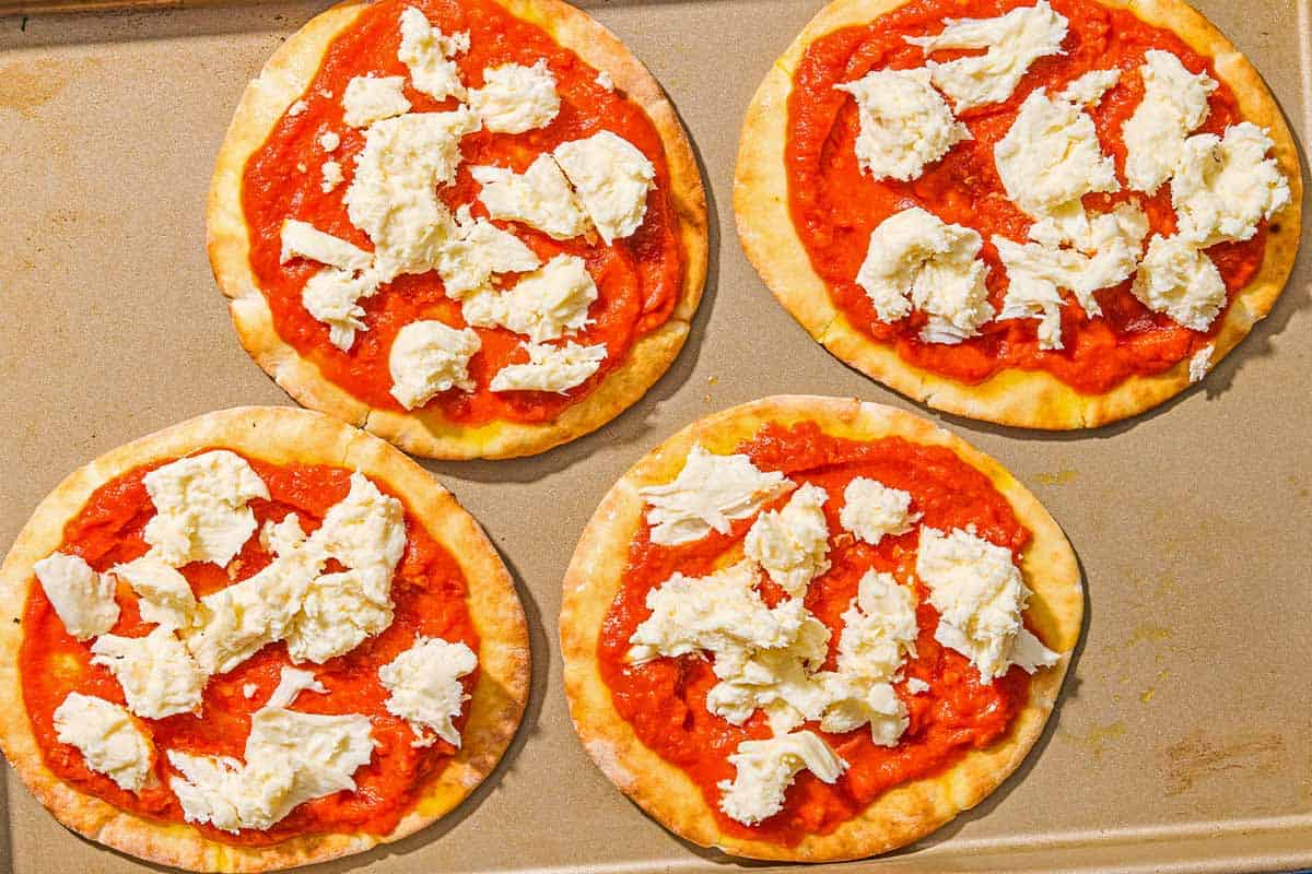 Four unbaked pita pizzas on a sheet pan.