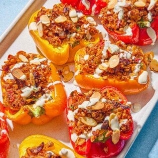 The quinoa stuffed peppers drizzled with tahini sauce in a baking dish.