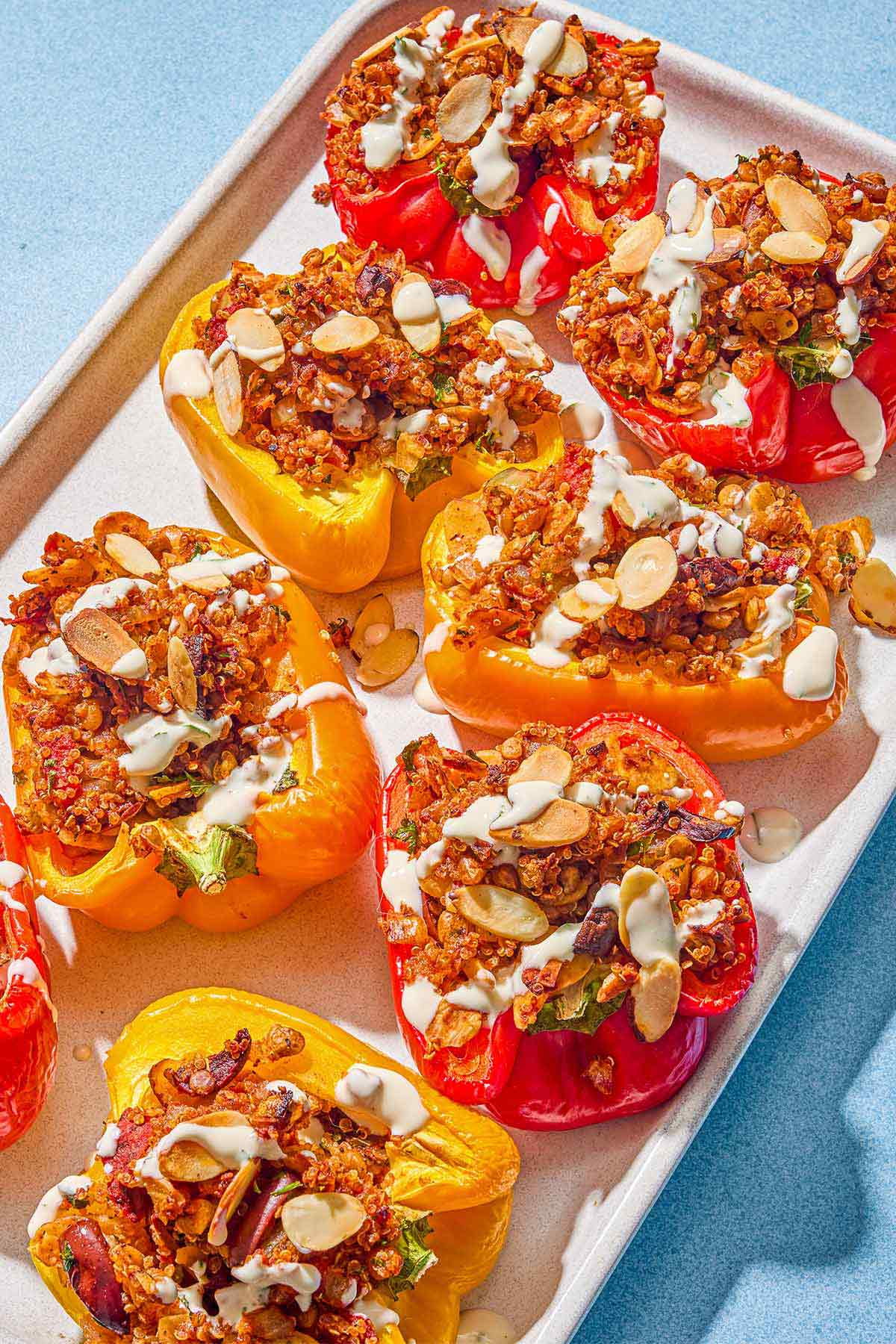 The quinoa stuffed peppers drizzled with tahini sauce in a baking dish.
