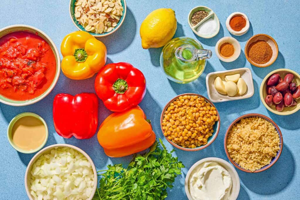 Ingredients for quinoa stuffed peppers including bell peppers, olive oil, onion, garlic, baharat, sweet paprika, cayenne pepper, fire roasted diced tomatoes, quinoa, lentils, almonds, kalamata olives, parsley, salt, tahini, lemon, garlic, and yogurt.