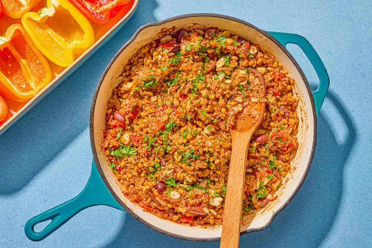 The stuffing for the quinoa stuffed peppers in a skillet with a wooden spoon. Next to this is a baking dish with the seeded pepper halves.