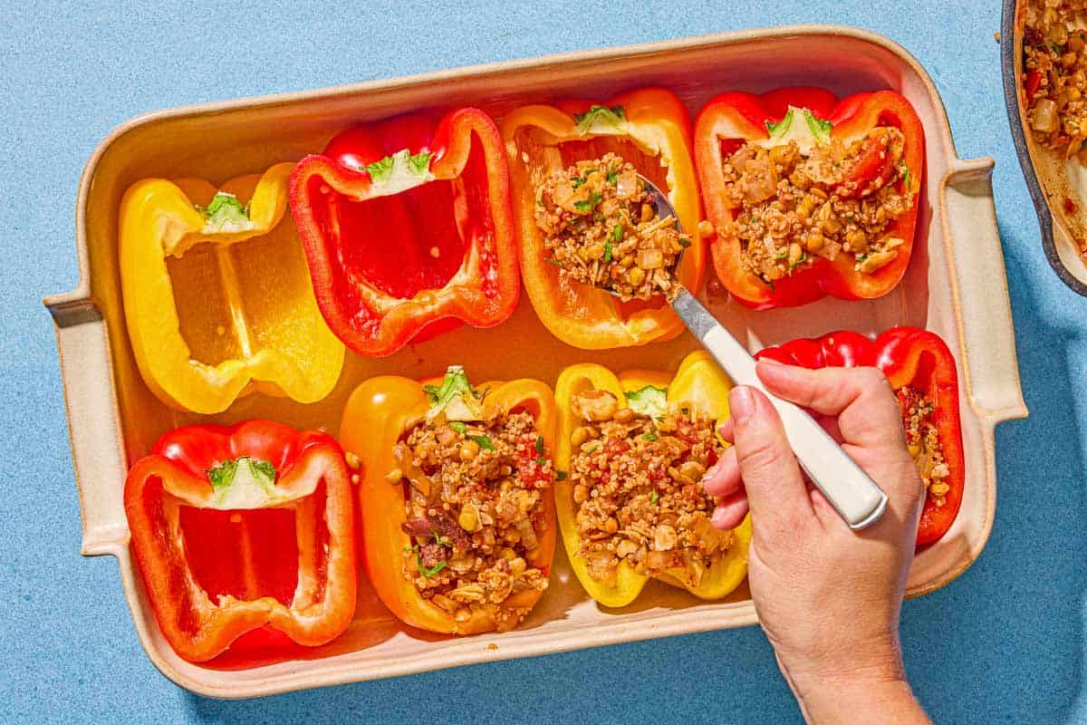 The stuffing for the quinoa stuffed peppers being spooned into the pepper halves in a baking dish.