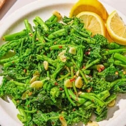 Broccoli rabe on a platter with lemon wedges.
