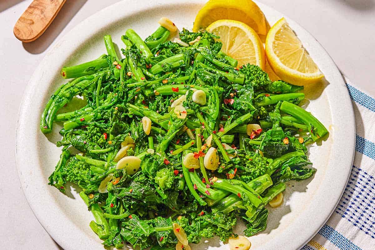 Broccoli rabe on a platter with lemon wedges.