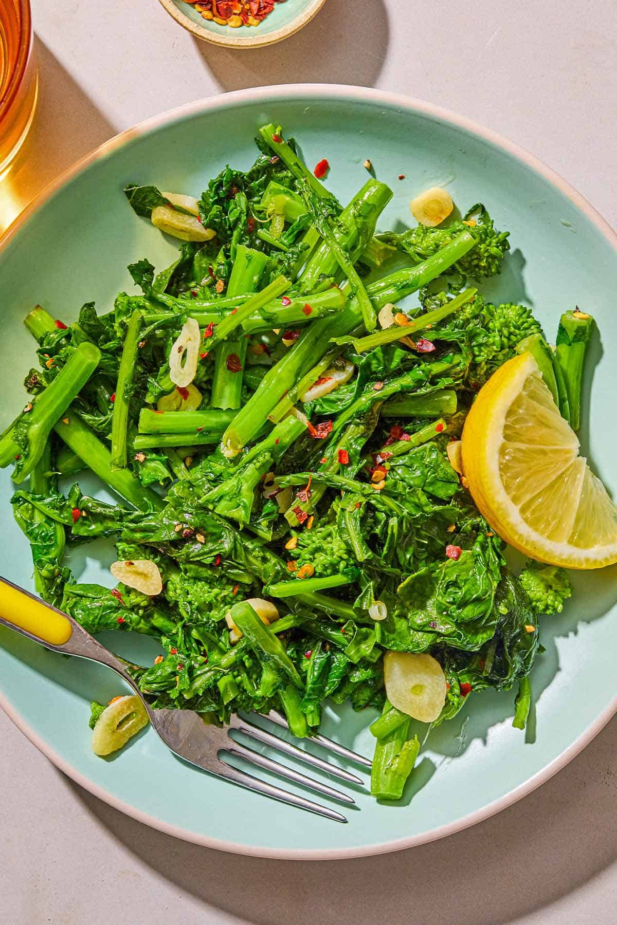 A serving of broccoli rabe on a plate with a lemon wedge and a fork.