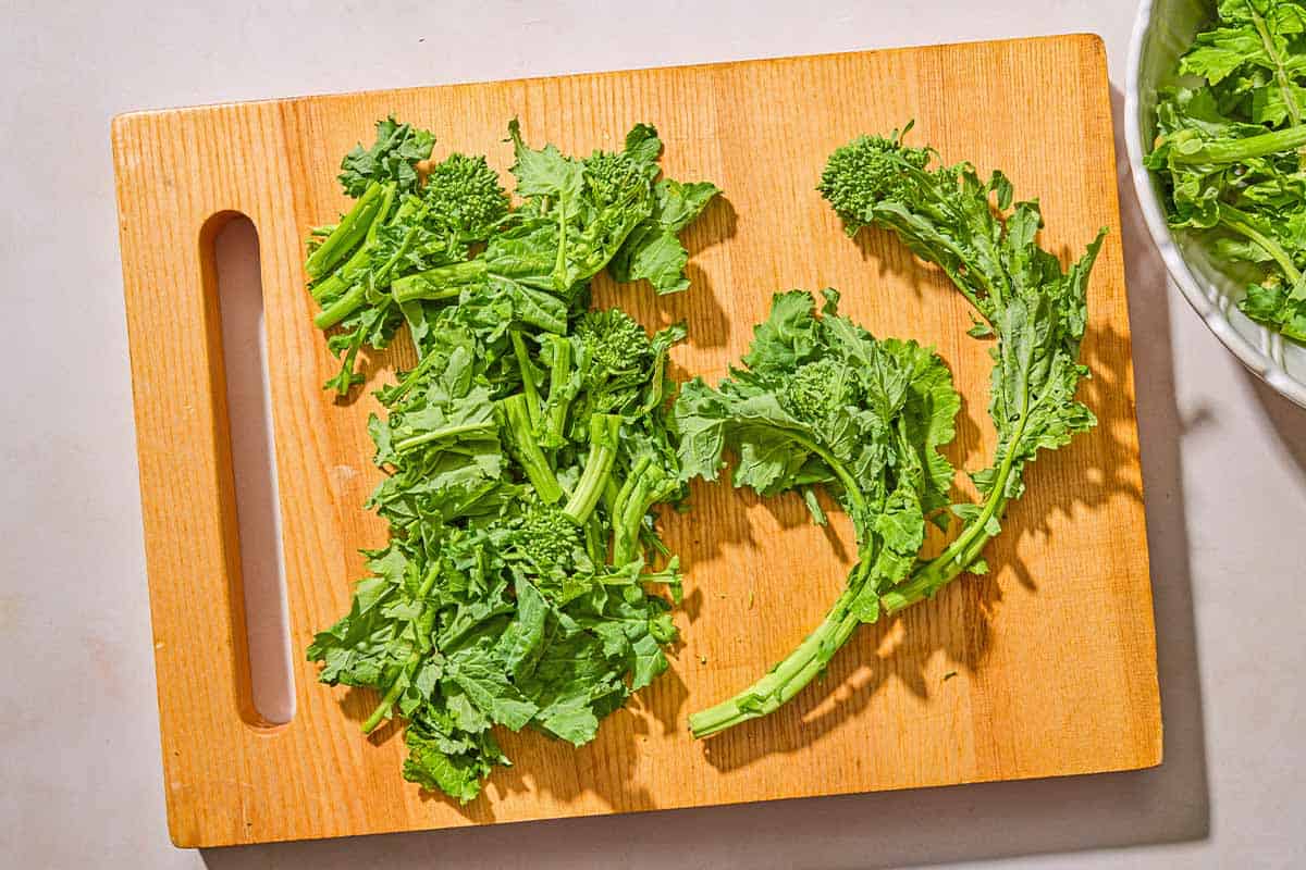Trimmed pieces of broccoli rabe on a cutting board. Next to this is a bowl with the rest of the broccoli rabe.