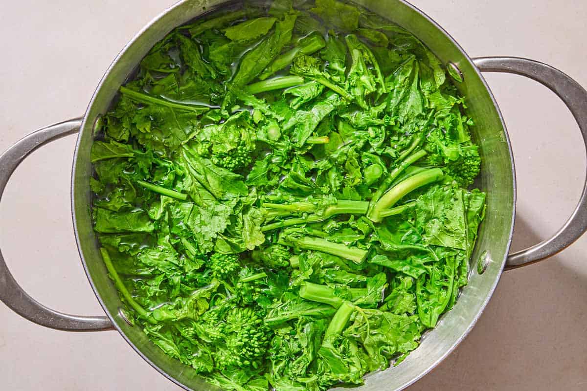 The broccoli rabe being blanched in a pot of water.